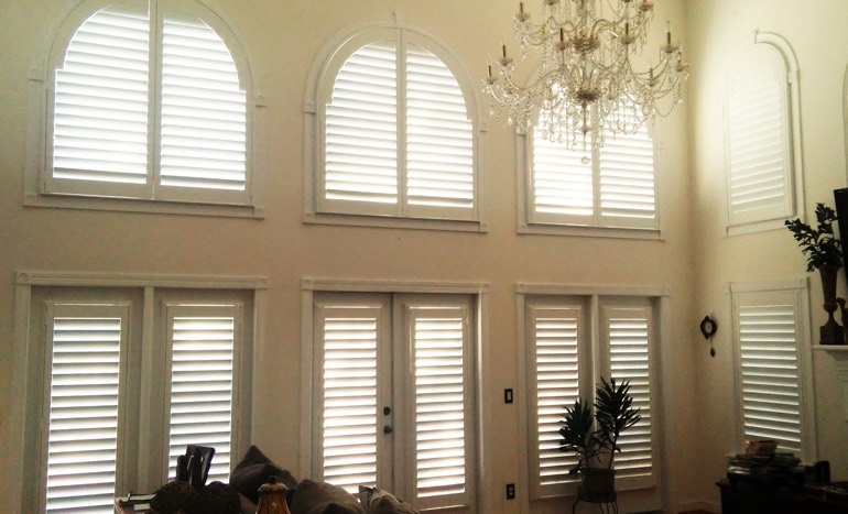 Entertainment room in open concept St. George home with plantation shutters on high ceiling windows.